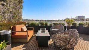 A rooftop terrace with a sofa, chairs, and a table, overlooking a cityscape. - Light-Filled Home in K-Town | Parking, Gym & Views (Los Angeles)