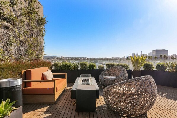 A rooftop terrace with a sofa, chairs, and a table, overlooking a cityscape.