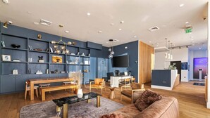 A modern reception area with a wooden reception desk, a seating area with a sofa and chairs, and a wall-mounted TV. - Light-Filled Home in K-Town | Parking, Gym & Views (Los Angeles)