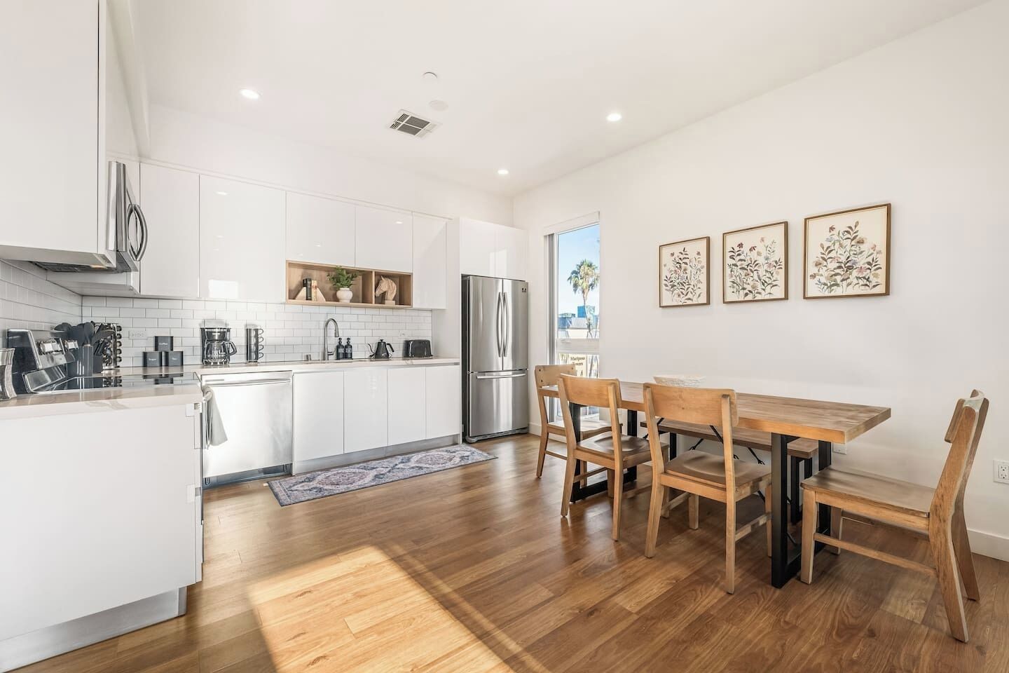 Une cuisine moderne avec des meubles blancs, des appareils en acier inoxydable et une table à manger en bois, accompagnée de chaises.