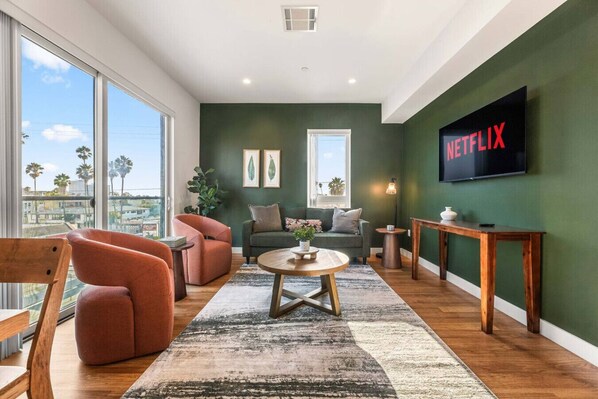 Moderni olohuone, jossa on yksi seinä maalattu vihreällä korostusvärillä, suuri ikkuna, sohva, sohvapöytä ja televisio, jonka näytöllä näkyy Netflixin logo.