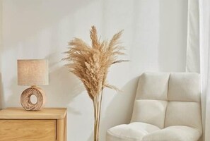 Ein Zimmer mit einem Nachttisch aus Holz, einer Lampe und einer hohen Pflanze.