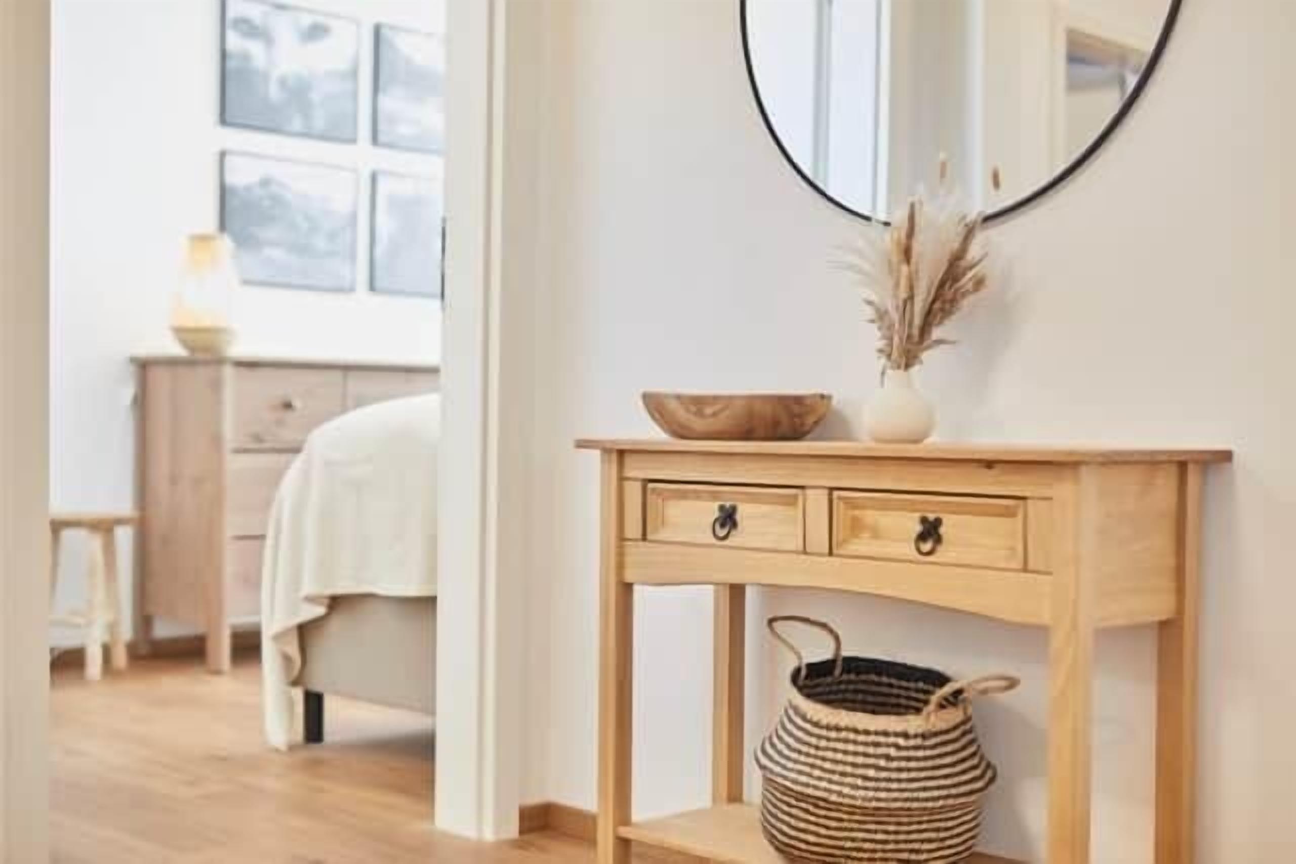 A wooden console table with a mirror, a vase with dried plants, and a woven basket.