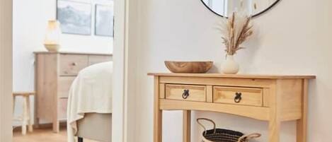A wooden console table with a mirror, a vase with dried plants, and a woven basket.