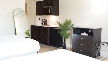 A compact bedroom with a bed, a small kitchenette, and a dark-colored dresser.