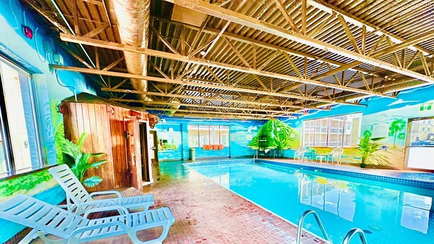 Una piscina interna con acqua cristallina, circondata da lettini e un pavimento piastrellato.
