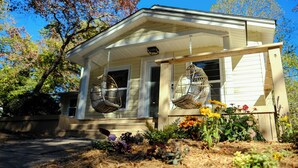 A house with a porch, two hanging birdcages, and a garden with various flowers. - Candler Cottage: Close 2 Everything "Asheville" (Candler)