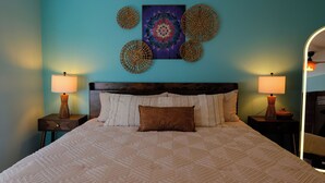 A bedroom with a large bed, two bedside tables with lamps, a wall-mounted artwork, and a mirror. - Candler Cottage: Close 2 Everything "Asheville" (Candler)