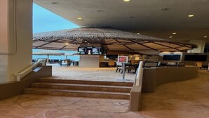 Ein Eingangsbereich mit Steinboden, einem Strohdachschirmchen, einer Bar und einer Treppe zu oberen Etagen.