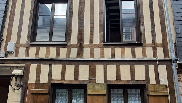 Ein zweistöckiges Gebäude mit traditioneller Fachwerkausfachung, zahlreichen Fenstern mit Fensterläden und einem sichtbaren Schornstein.
