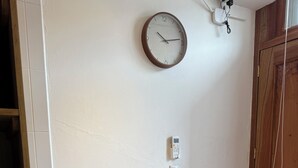 Pieni ruokailutila, jossa on pyöreä pöytä, kaksi tuolia, seinäkello ja seinälle asennettu termostaatti.