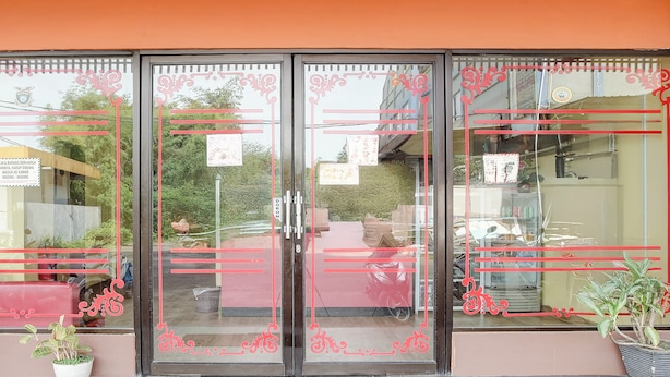 L’entrée d’un hôtel avec des portes en verre, des motifs décoratifs rouges et des plantes en pot.