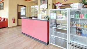 Un espace d’accueil avec un comptoir rose, une vitrine réfrigérée contenant des boissons et une horloge au mur.
