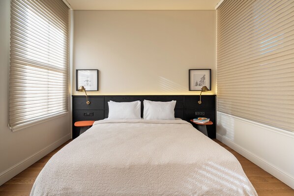 A neatly made bed with a white textured blanket, two bedside tables with lamps, and framed artwork on the walls.
