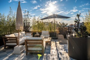 A rooftop terrace with outdoor seating, a large umbrella, and a potted plant.