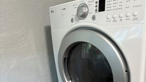 Eine Frontlader Waschmaschine und Trocknerkombination mit Bedienfeld, vor einer hellgrauen Wand und Holzdielen.