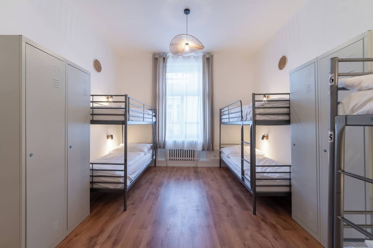 A dormitory room with bunk beds, a radiator, and a window with curtains.