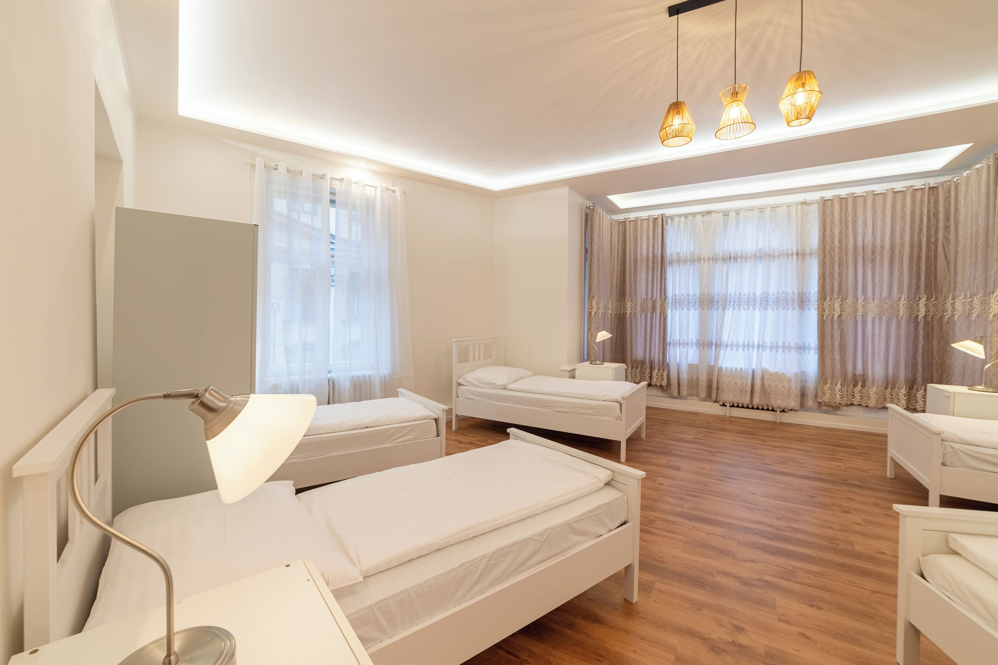 Een hotelkamer met twee enkele bedden, een nachtkastje met een lamp, een grote spiegel en een plafondlamp.