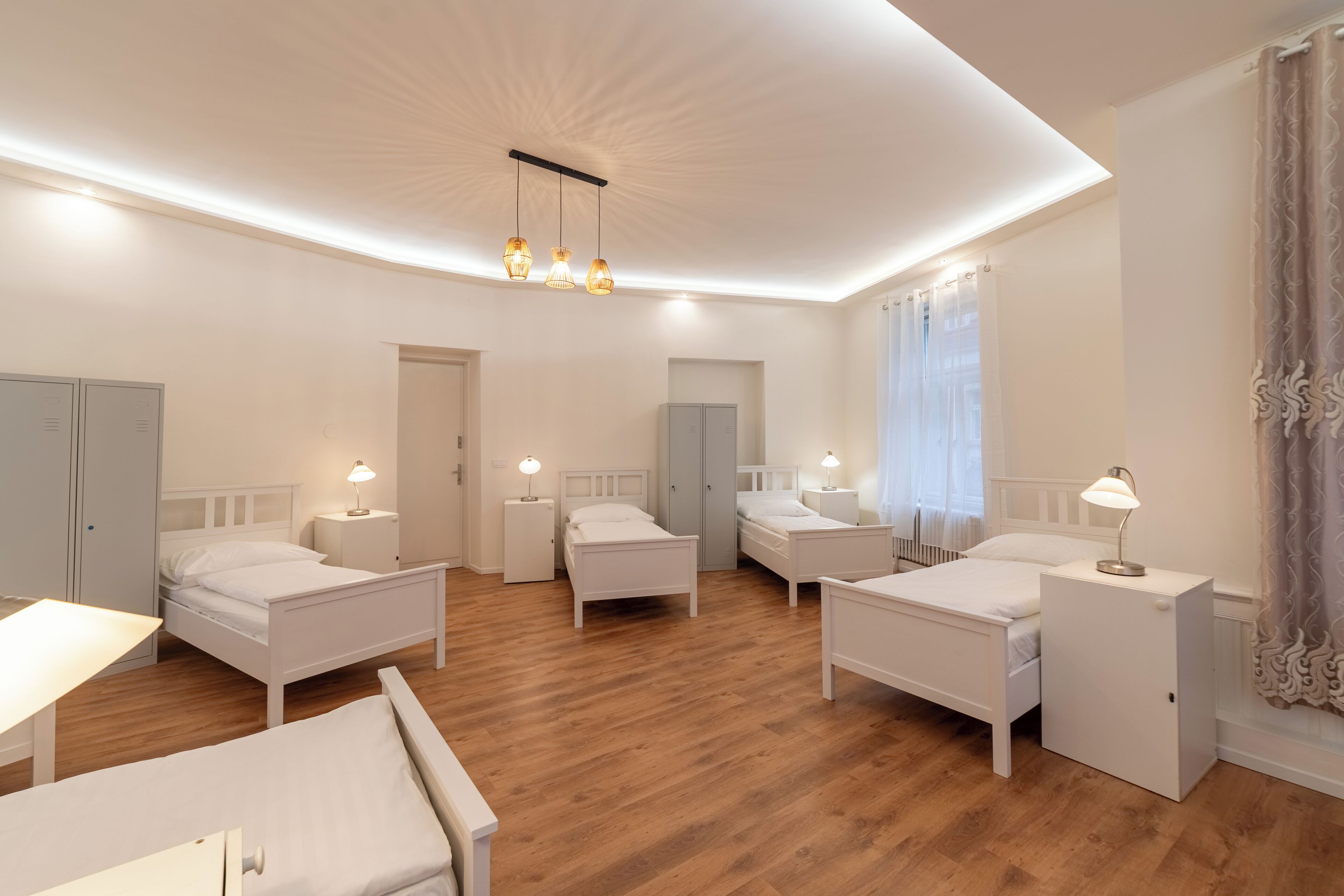 A modern hotel room with four single beds, a desk, and a small table.