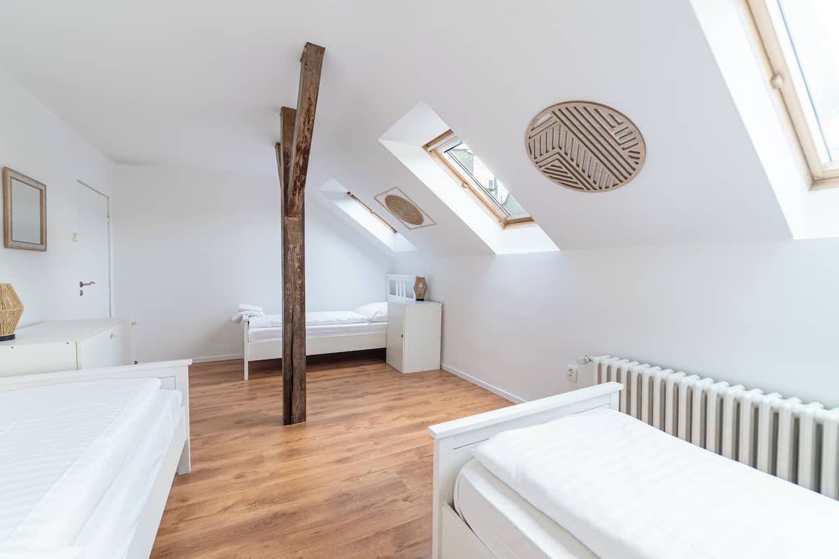 A bedroom with a sloped ceiling, skylights, a wooden beam, a white bed, a white dresser, and a white radiator.
