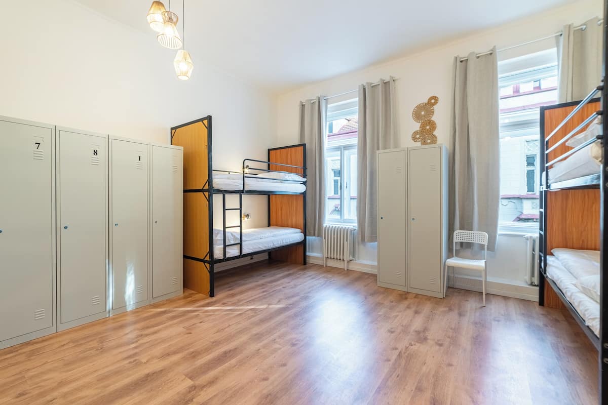 A dormitory room with bunk beds, lockers, a radiator, and a window with curtains.
