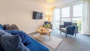 A modern living room with a sofa, armchair, coffee table, and a TV mounted on the wall. - Modern 2BR Apartment with Water Views (Cardiff)