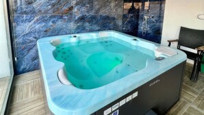 Un baño moderno con pared de mármol, una bañera independiente y suelo de madera.