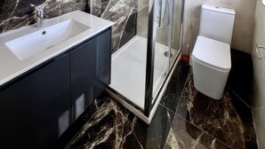 Un baño moderno con ducha envuelta en vidrio, un lavamanos blanco y un inodoro.