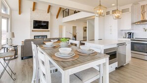 Cozinha moderna com ilha central, eletrodomésticos embutidos e área de jantar com mesa e cadeiras de madeira.