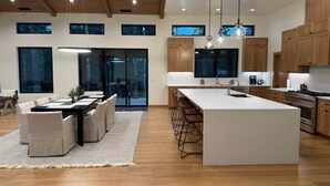 Moderni keittiö, jossa on puiset kaapit, suuri keittiösaareke ja riippuvalaisimet.