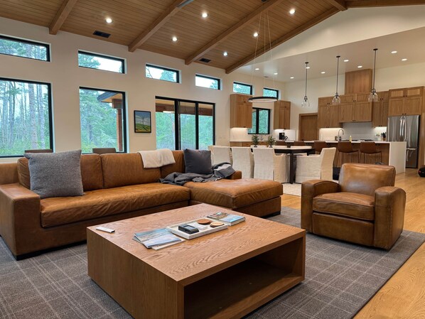 A spacious living room with a brown leather sofa, a wooden coffee table, and a dining area with a kitchen in the background. - Bandon Heath - Walk to Bandon Dunes Golf Resort (Bandon)