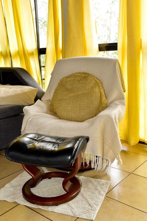 Une chaise dotée d’un coussin d’assise tissé, d’un repose-pieds en cuir et d’un plaid blanc.