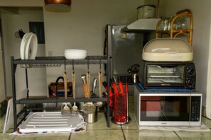 Une cuisine équipée d’un four à micro-ondes, d’un grille-pain et d’une étagère contenant de la vaisselle et des ustensiles.