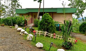 A building with a green roof, a wooden fence, and a garden with rocks and plants. - SauGaLe - Near Chirripó, King Bed, Pool & Hot Tub (Pérez Zeledón)