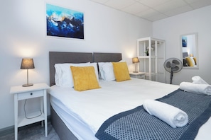 Ein Hotelzimmer mit einem Bett, Nachttischlampen, einem Ventilator, einem Spiegel und einem Gemälde an der Wand.