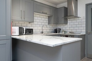 A modern kitchen with grey cabinets, a white marble countertop, a stainless steel range hood, a microwave, a toaster, and a coffee maker.
