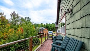 Un patio in legno con posti a sedere all'aperto, un barbecue e vista su una baita in una zona boschiva.