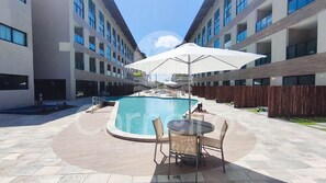 Ein Swimmingpool mit Sonnenschirm, umgeben von einer gepflasterten Terrasse mit Sitzgelegenheiten.