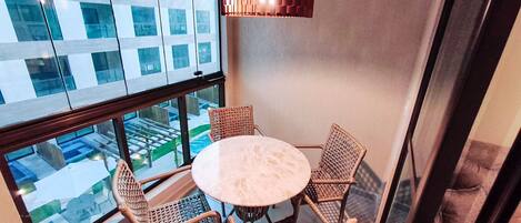 A balcony with a round table and four wicker chairs, overlooking a cityscape.