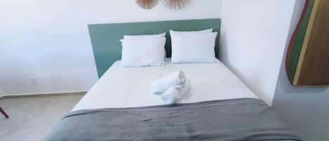 A bed with white linens, a grey blanket, and a rolled towel.