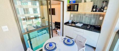 Una pequeña cocina con microondas, tostadora y cafetera. Hay una mesa de comedor con platos azules y blancos y una silla.