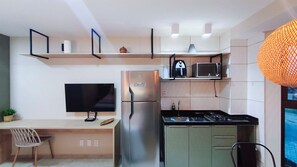 Eine kompakte Küche mit Kühlschrank, Mikrowelle und Herd, einem Flachbildfernseher und einem Essbereich mit Stuhl und Tisch.