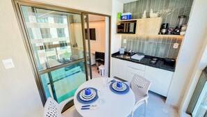 Een kleine keuken met een magnetron, broodrooster en koffiezetapparaat. Er staat een eettafel met blauwe en witte borden en een stoel.