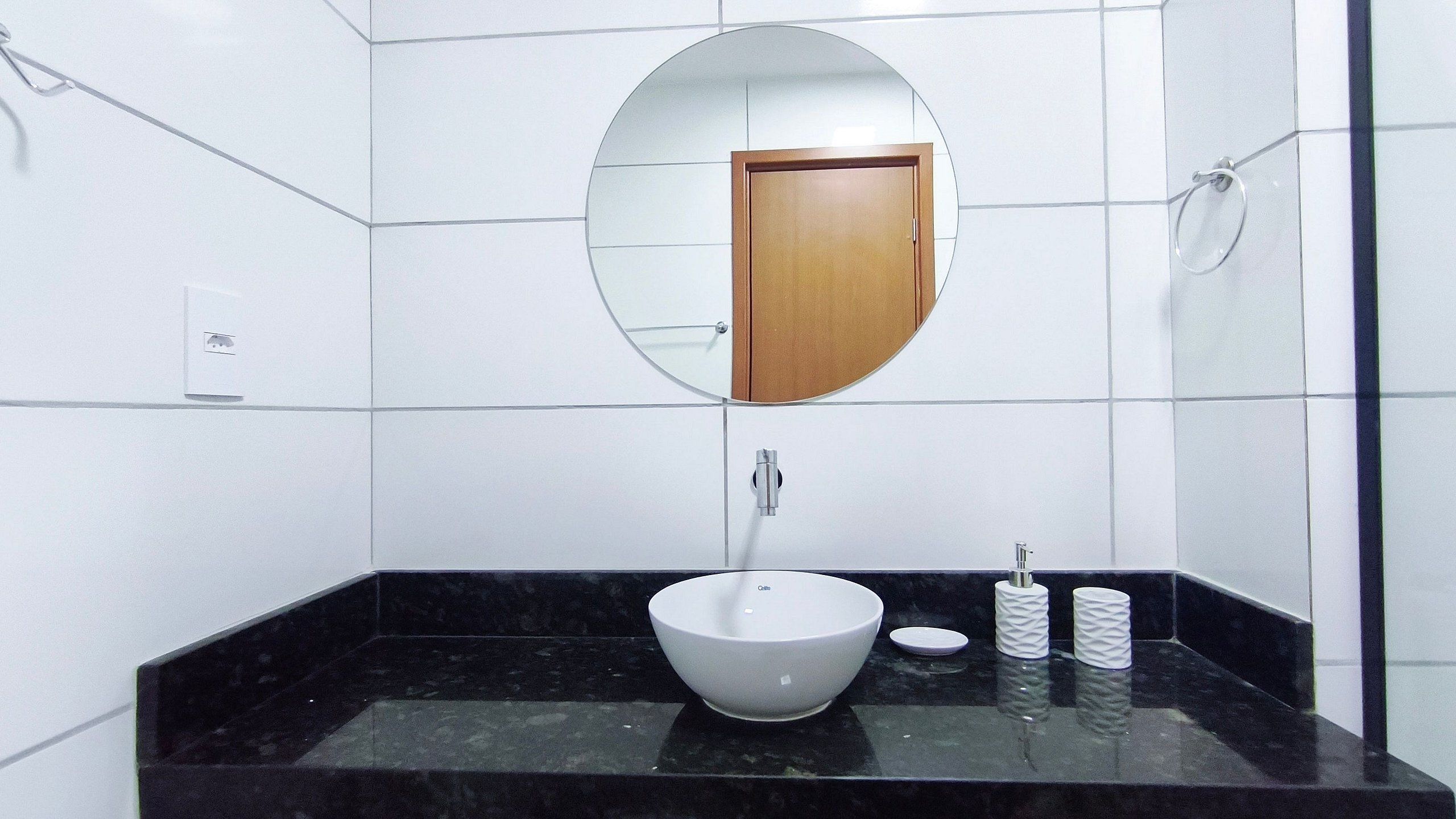 Un baño con un lavabo blanco, un espejo redondo y una puerta de madera.