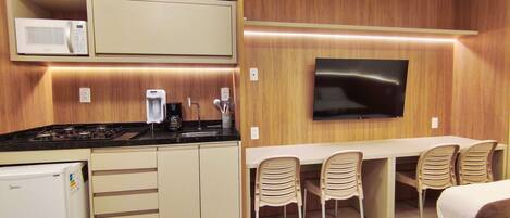A compact kitchen with a microwave, coffee maker, and stove. There is a dining area with a TV and four chairs.