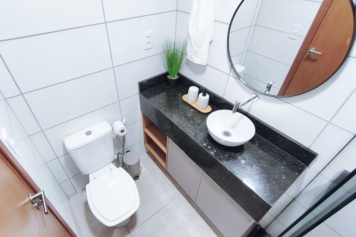 Une salle de bain équipée de toilettes, d’un lavabo, d’un miroir et d’une plante en pot.
