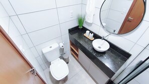 Une salle de bain équipée de toilettes, d’un lavabo, d’un miroir et d’une plante en pot.