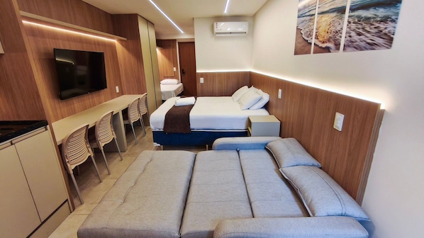 Een kleine hotelkamer met een bed, televisie, bureau en stoelen.