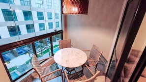 Een balkon met een ronde tafel en vier rieten stoelen, met uitzicht op een stadsgezicht.