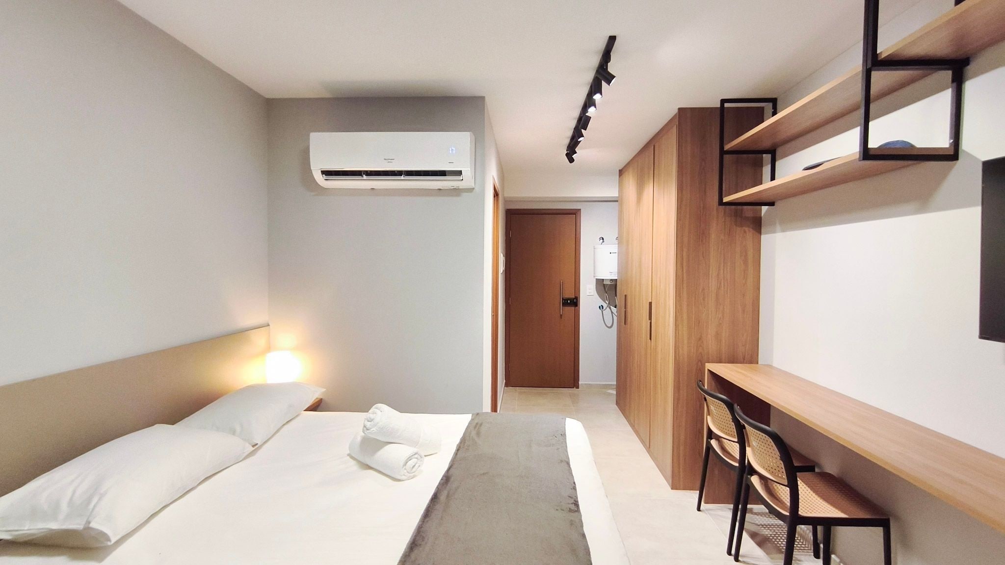 Una habitación de hotel con cama, mesita de noche, silla, escritorio y un equipo de aire acondicionado.